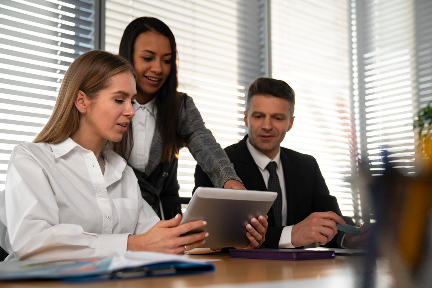 Three professionals collaborating in an office, reviewing content on a tablet during a team meeting.