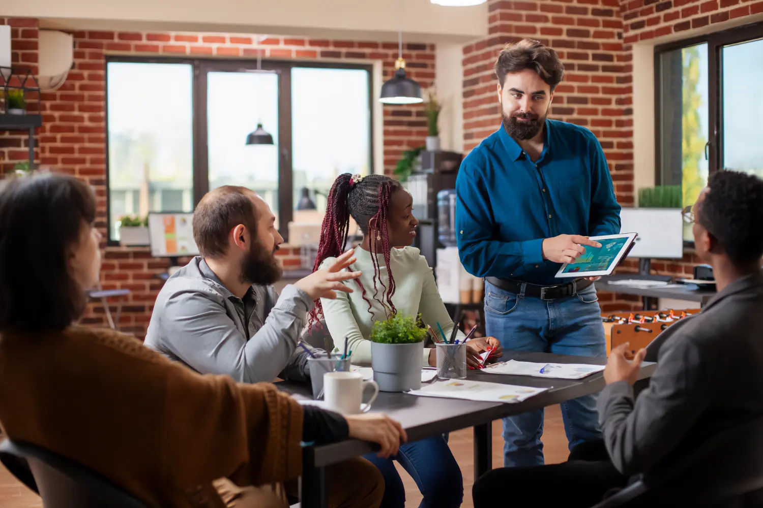 Diverse business team in a modern office discussing recruitment data displayed on a tablet, collaborating on candidate evaluation strategies.