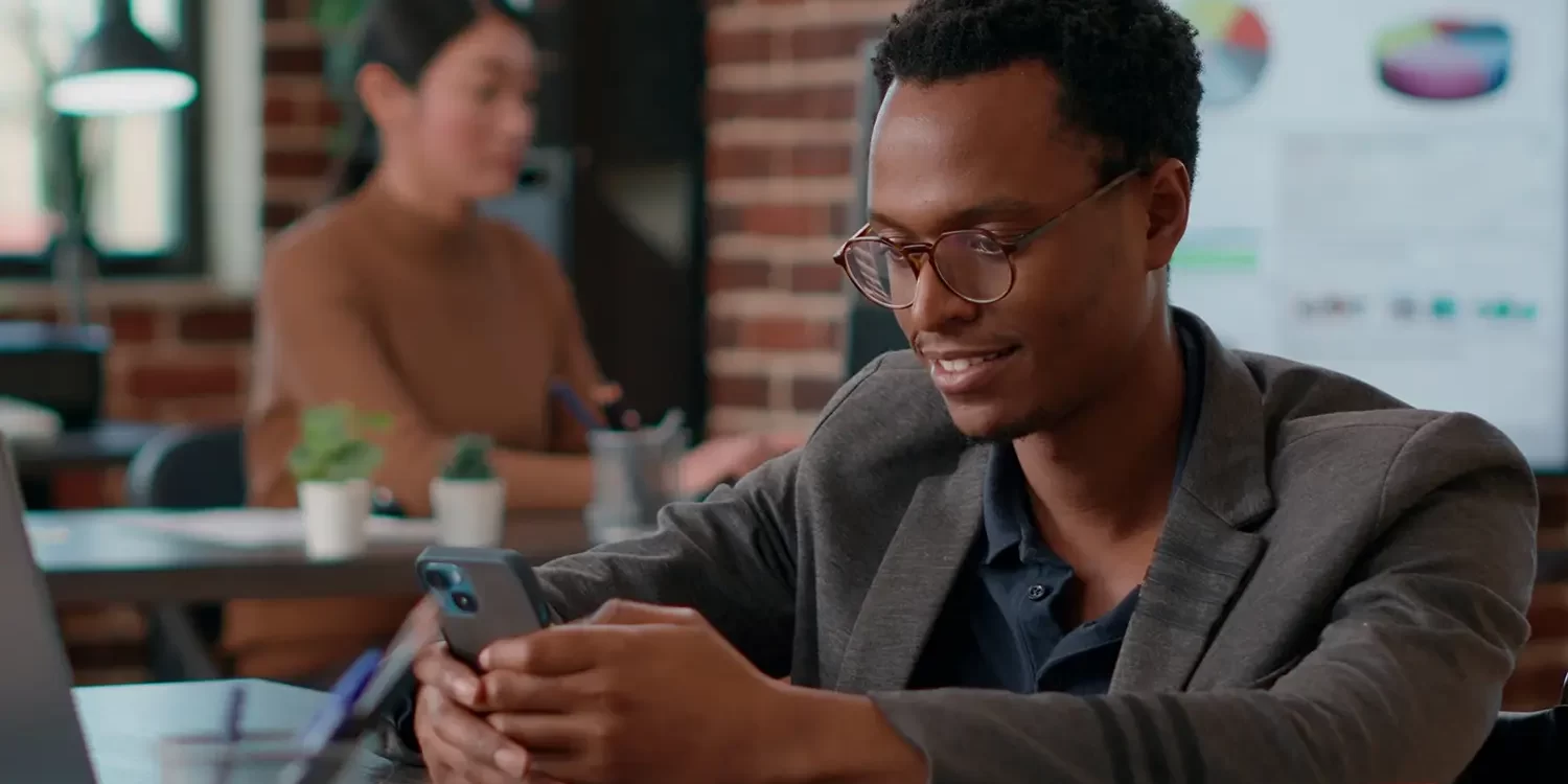 Smiling businessman checking his phone in modern office, using mobile recruitment app for candidate search and matching.