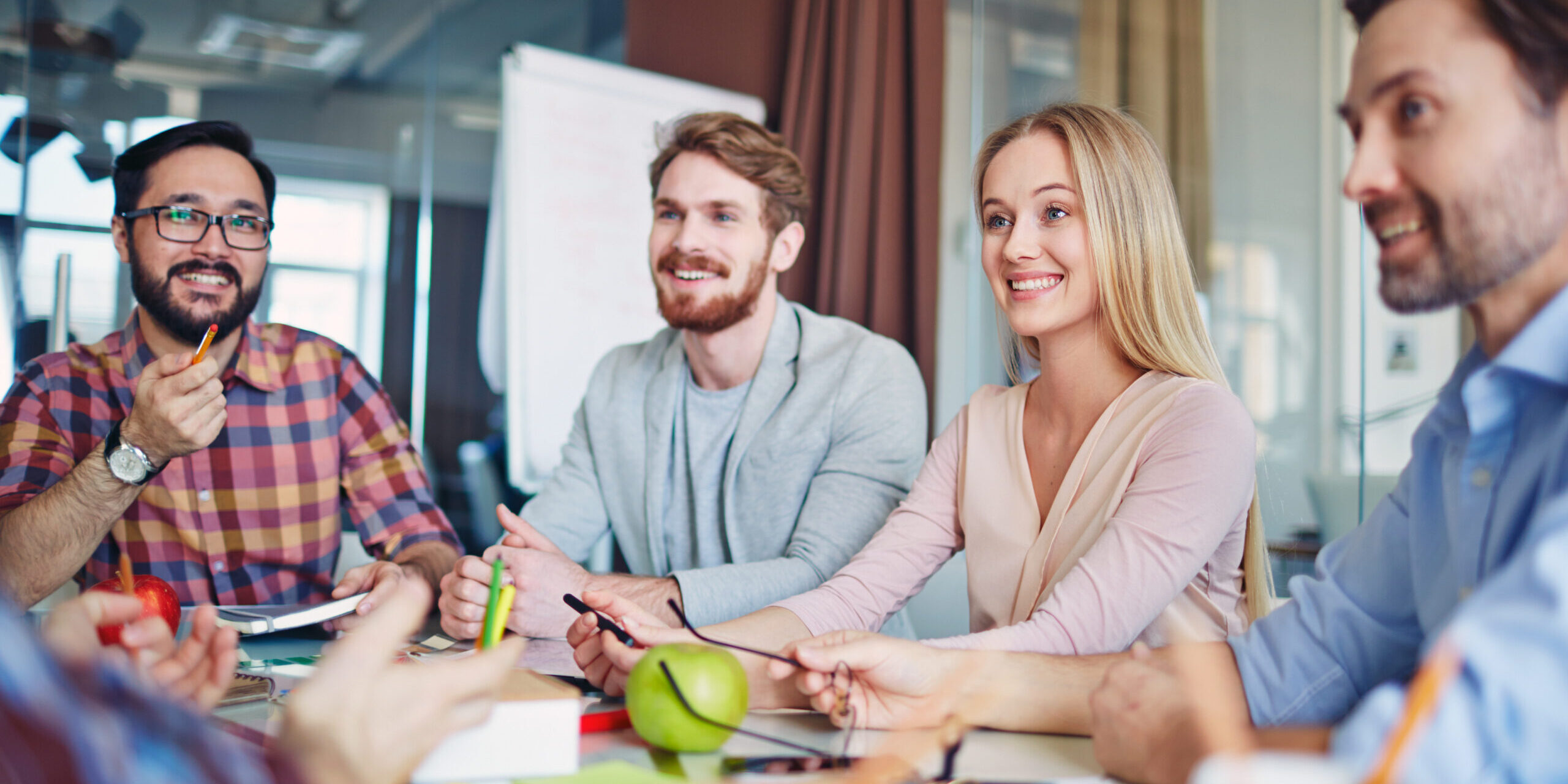 Group of professionals smiling during a collaborative meeting in a modern office setting.