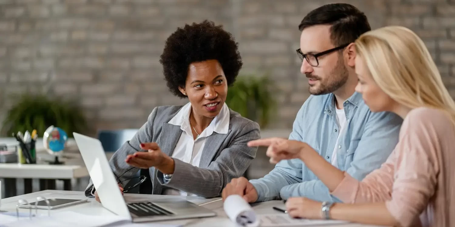 Team of recruiters collaborating on candidate evaluations during hiring process with laptop in office.